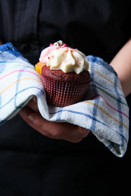 Gratis foto verticale opname van een persoon met twee cupcakes op een keukenhanddoek