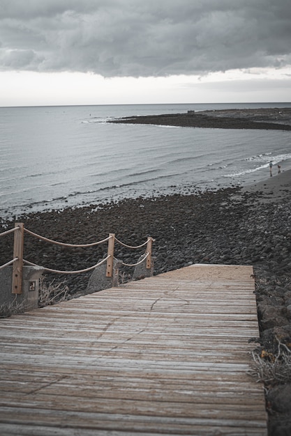 Gratis foto verticale opname van een strand met een houten brug onder bewolkte hemel