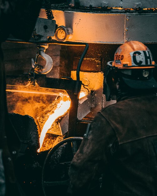 Verticale opname van een volwassen fabrieksarbeider in uniform die metaal smelt in een fabriek