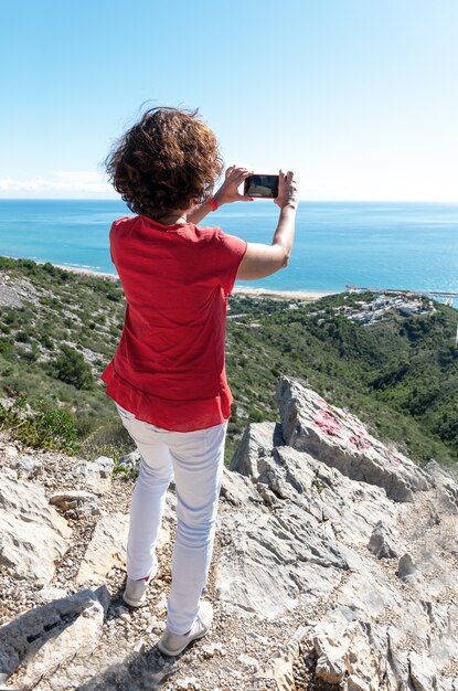 Verticale opname van een vrouw die op rotsen staat en de prachtige zee fotografeert