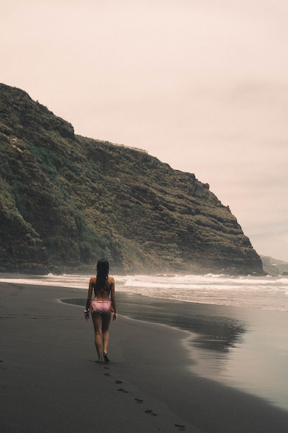 Gratis foto verticale opname van een vrouw op het strand met kliffen