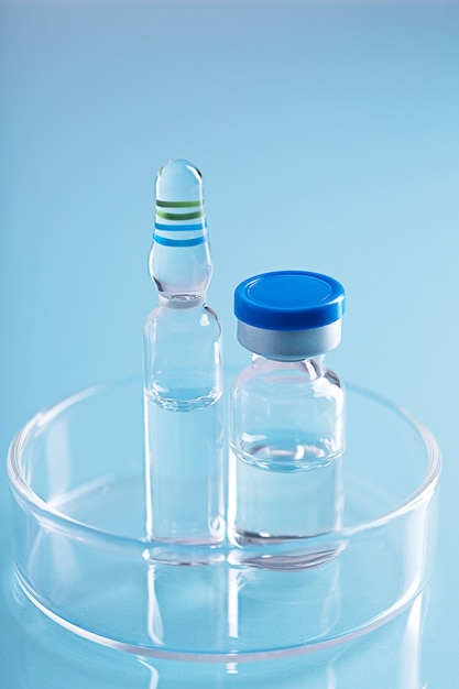 Verticale opname van twee verschillende glazen flesjes met heldere vloeistof in een glazen schaal op blauw oppervlak blue
