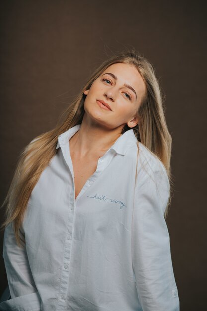 Verticale shot van een aantrekkelijke blonde vrouw in een wit overhemd poseren op een bruin oppervlak