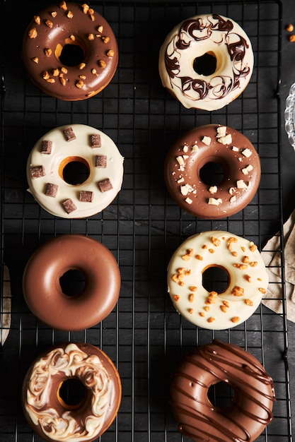 Verticale shot van heerlijke donuts bedekt met de witte en bruine chocolade glazuur op een zwarte tafel