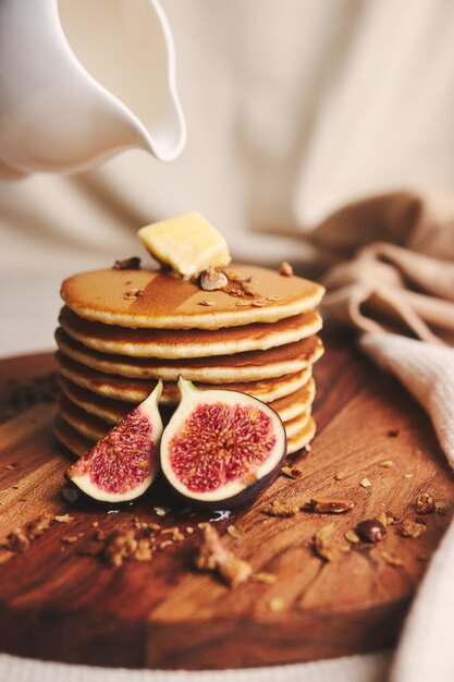 Verticale shot van pannenkoeken met stroop, boter, vijgen en geroosterde noten op een houten plaat