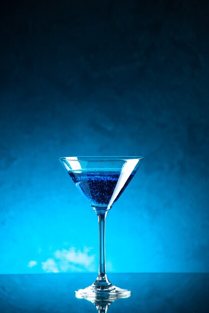 Verticale weergave van blauw water in een glazen beker aan de rechterkant op een donkere achtergrond