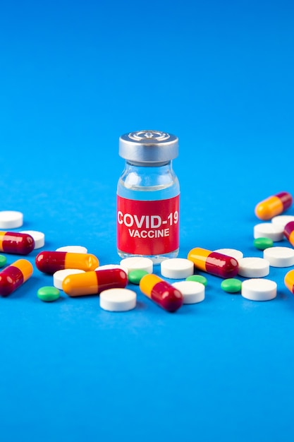 Verticale weergave van covid-vaccin in medische ampul pillen capsules op donkere en zachte blauwe achtergrond