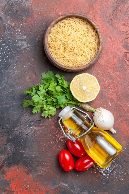 Verticale weergave van de achtergrond van het diner, ongekookte pasta's, citroen, een bos groene oliefles op een donkere achtergrond