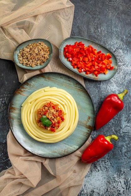 Verticale weergave van een blauw bord met smakelijke pastamaaltijd geserveerd met tomaat en vlees op een bruine handdoek, gehakte en hele paprika's