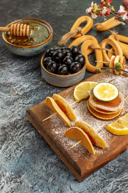 Verticale weergave van fruit pannenkoeken koekjes in de buurt van honing in een kom en zwarte kersen op grijze tafel