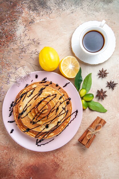 Verticale weergave van gemakkelijke pannenkoeken versierd met chocoladesiroop met lemonnd thee op kleurrijke tafel