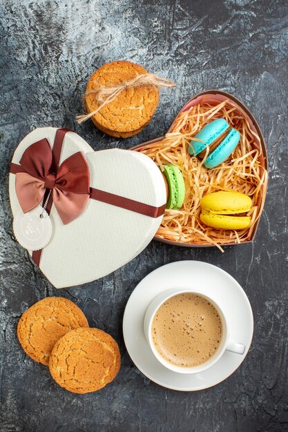 Verticale weergave van geschenkdoos met macarons en koekjes een kopje koffie op ijzige donkere achtergrond