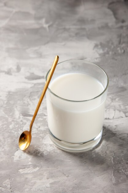 Verticale weergave van glazen beker gevuld met melk en gouden lepel op grijze tafel met vrije ruimte