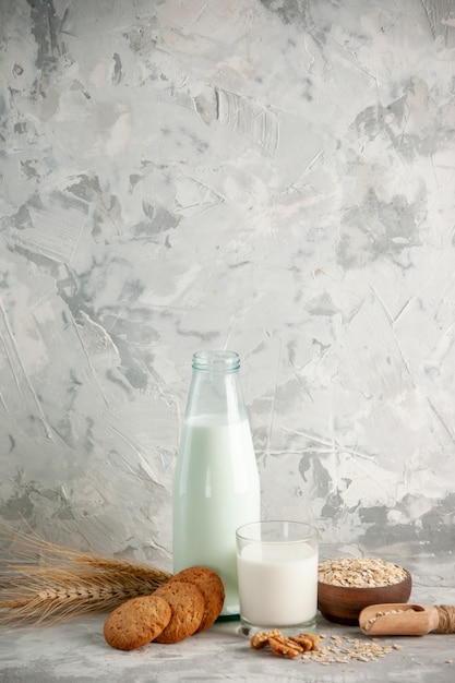 Verticale weergave van glazen fles en beker gevuld met melk op houten dienblad en koekjeslepel haver in bruine pot op witte tafel op ijsachtergrond