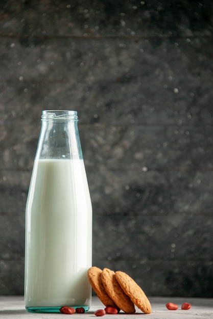 Verticale weergave van glazen fles gevuld met melk en pinda's op grijze tafel op houten achtergrond