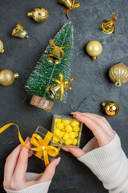 Verticale weergave van hand met geschenkdozen en kerstboom decoratie accessoires op donkere achtergrond