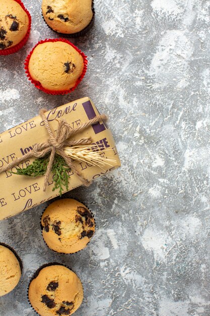 Verticale weergave van heerlijke kleine cupcakes met chocolade en dennentakken naast cadeau op ijsoppervlak