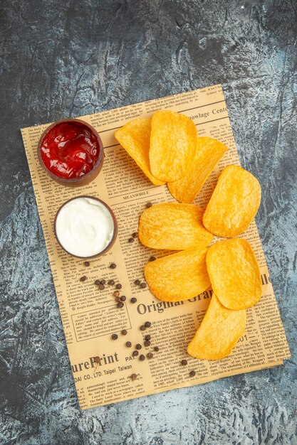 Verticale weergave van heerlijke zelfgemaakte chips en peper kom mayonaise ketchup en saus op krant op grijze tafel