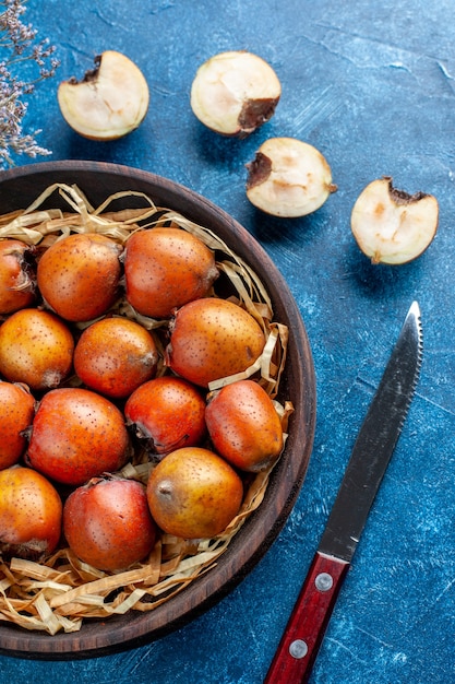 Verticale weergave van hele en gehakte mespilus germanica binnen en buiten een bruine kom naast vork op blauwe achtergrond