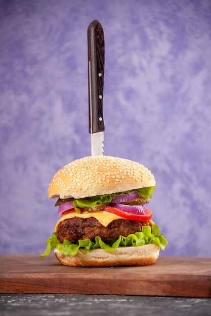 Verticale weergave van mes in smakelijke sandwich met vlees op houten snijplank op geïsoleerde ijsoppervlak