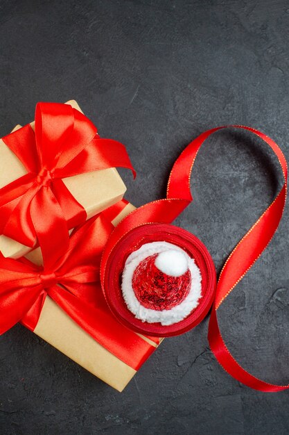 Verticale weergave van mooie geschenken met rood lint en kerstman hoed op donkere tafel