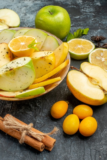 Verticale weergave van natuurlijke appels, citroen op een witte plaat en kaneel limoenen kumquats sinaasappels op donkere tafel