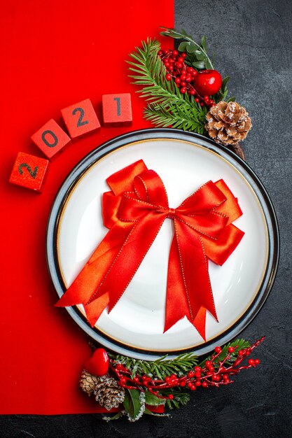 Verticale weergave van Nieuwjaar achtergrond met rood lint op diner plaat decoratie accessoires fir takken en getallen op een rood servet op een zwarte tafel