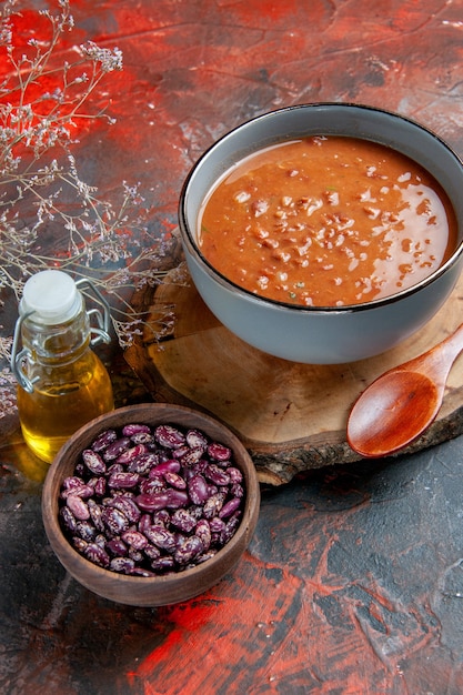 Gratis foto verticale weergave van tomatensoep in een blauwe kom op een houten dienblad bonen olie fles op gemengde kleurentafel