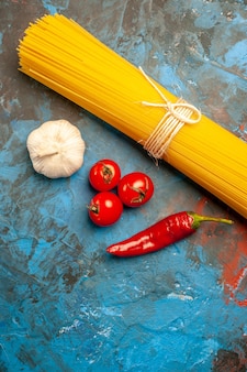 Verticale weergave van vermicelli pasta's vastgebonden met touw en tomaten peper knoflook op blauwe achtergrond