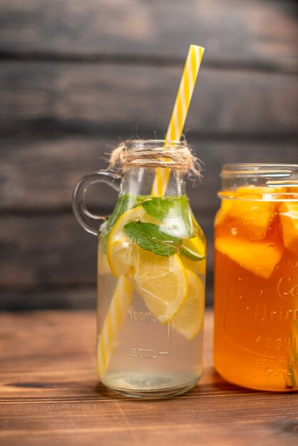 Verticale weergave van vers detoxwater en vruchtensap geserveerd met buizen aan de linkerkant op een bruine achtergrond