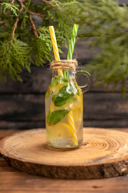 Verticale weergave van vers detoxwater in een glas geserveerd met buizen op een bruin dienblad