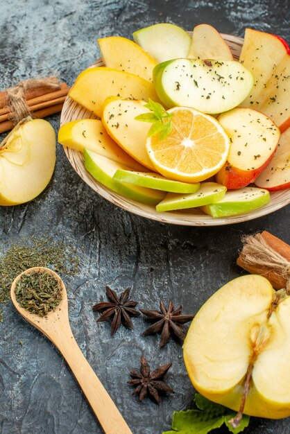 Verticale weergave van verse natuurlijke appelschijfjes op een witte plaat met citroen en kaneel limoenen kumquats sinaasappels op grijze achtergrond