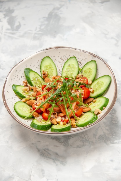 Verticale weergave van zelfgemaakte gezonde heerlijke veganistische salade versierd met gehakte komkommers in een kom op gekleurd wit oppervlak