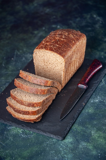 Verticale weergave van zwart brood sneetjes mes op donkere kleur bord op gemengde kleuren noodlijdende achtergrond