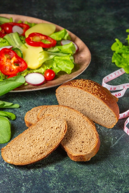 Gratis foto verticale weergave van zwart brood sneetjes vers gehakte groenten op een plaat en meter groene bundel op donkere kleuren oppervlak