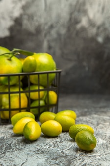 Verticale weergave van zwarte mand met verse groene mandarijnen en kumquats op grijze achtergrond