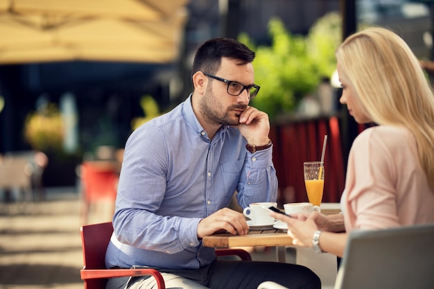 Verveelde man kijkt met argwaan naar zijn vriendin die sms't op mobiele telefoon en negeert hem in een café