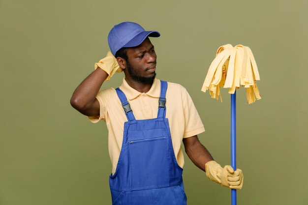 verward bedrijf mop jonge Afro-Amerikaanse schonere man in uniform met handschoenen geïsoleerd op groene achtergrond