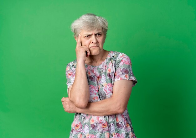 Verward oudere vrouw legt hand op kin kijken kant geïsoleerd op groene muur