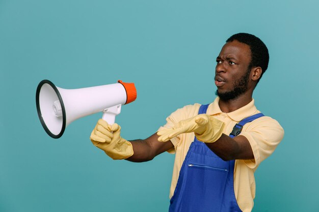 Verward spreekt op luidspreker jonge Afro-Amerikaanse schonere man in uniform met handschoenen geïsoleerd op blauwe achtergrond