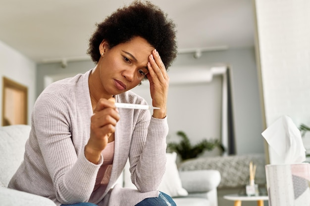 Verwarde Afro-Amerikaanse vrouw met hoofdpijn die haar temperatuur thuis meet