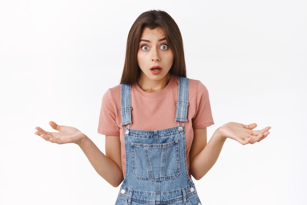 Verwarde geschokte vrouw die verontrust hijgt, iets uitlegt of slecht nieuws ontvangt, handen zijwaarts spreidt in ontzetting, staren camera verbaasd en verontrust, staande witte achtergrond