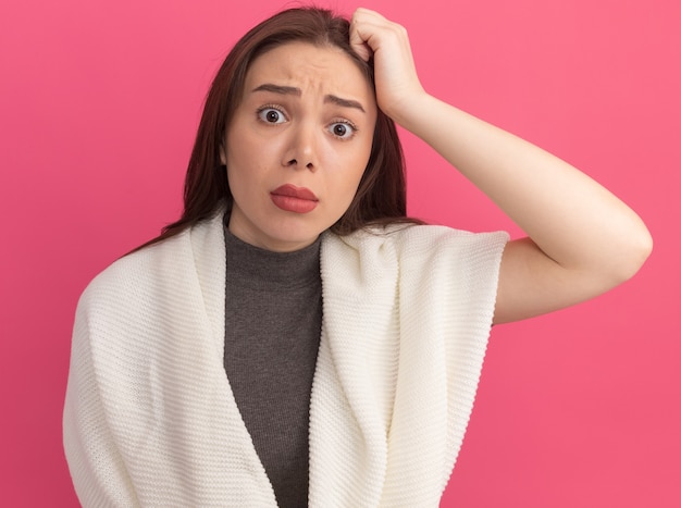 Verwarde jonge mooie vrouw die hand op het hoofd houdt geïsoleerd op roze muur