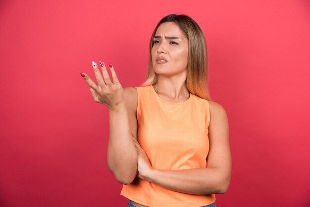 Verwarde jonge vrouw die haar hand zijwaarts op rode muur richt.