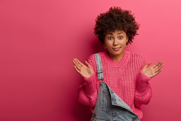 Verwarde, onbewuste vrouw met afro-kapsel, spreidt de handpalmen zijwaarts