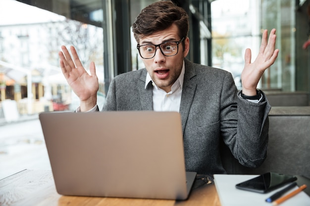 Verwarde zakenman in oogglazen die door de lijst in koffie zitten en laptop computer bekijken