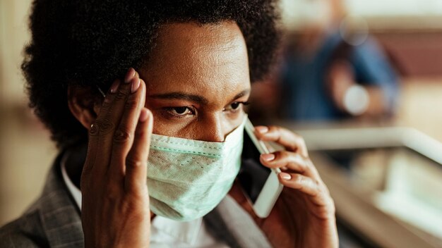 Verwarde zwarte zakenvrouw die via mobiele telefoon communiceert terwijl ze een beschermend masker draagt tijdens een virusepidemie