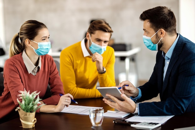 Verzekeringsagent en een stel gebruiken touchpad terwijl ze gezichtsmaskers dragen tijdens de vergadering