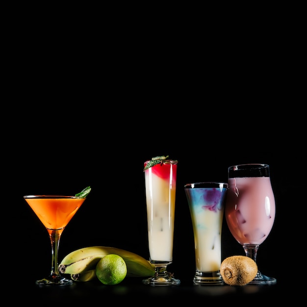 Vier cocktails en exotisch fruit op zwarte achtergrond