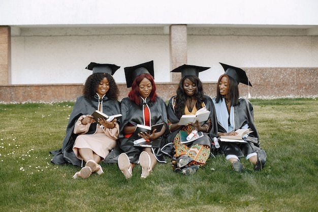 Vier jonge afro-amerikaanse vrouwelijke studenten gekleed in zwarte afstudeerjurk. campus als achtergrond